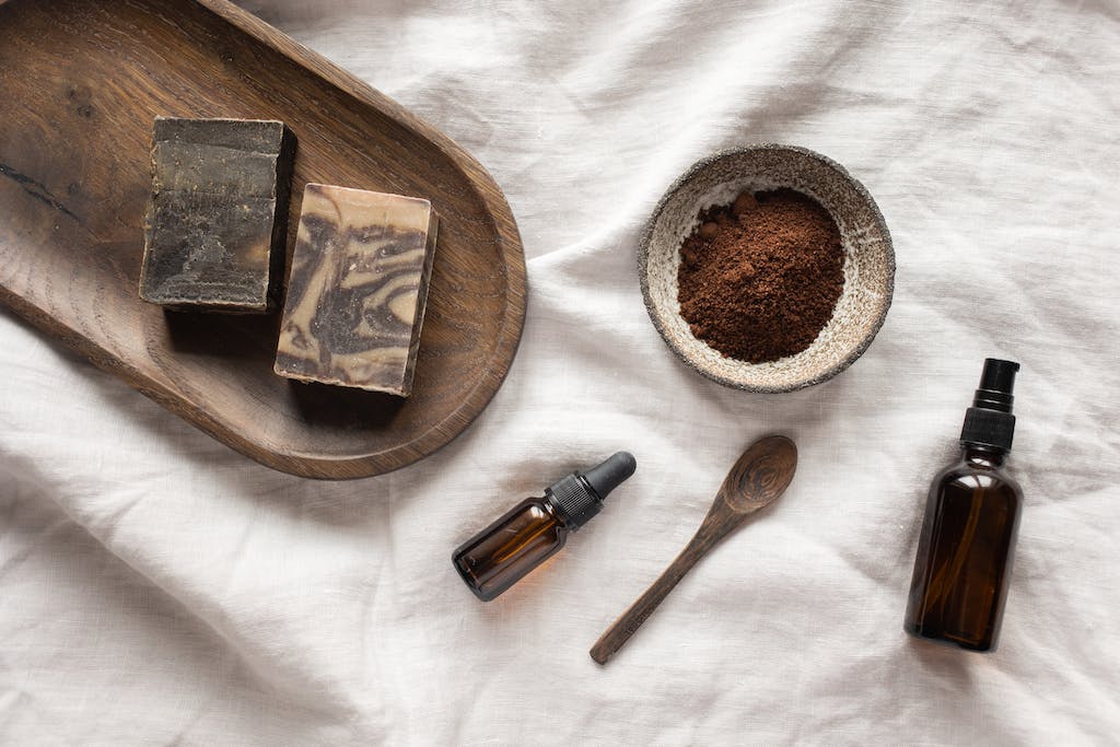 Top view of coffee scrub in bowl composed with bottles of aromatic oil on white sheet